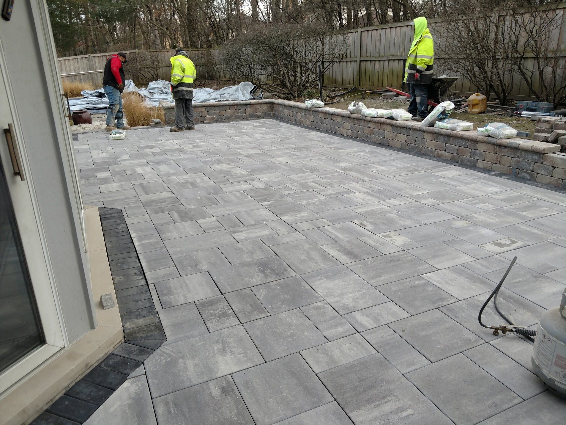 Workers laying gray paver patio in backyard